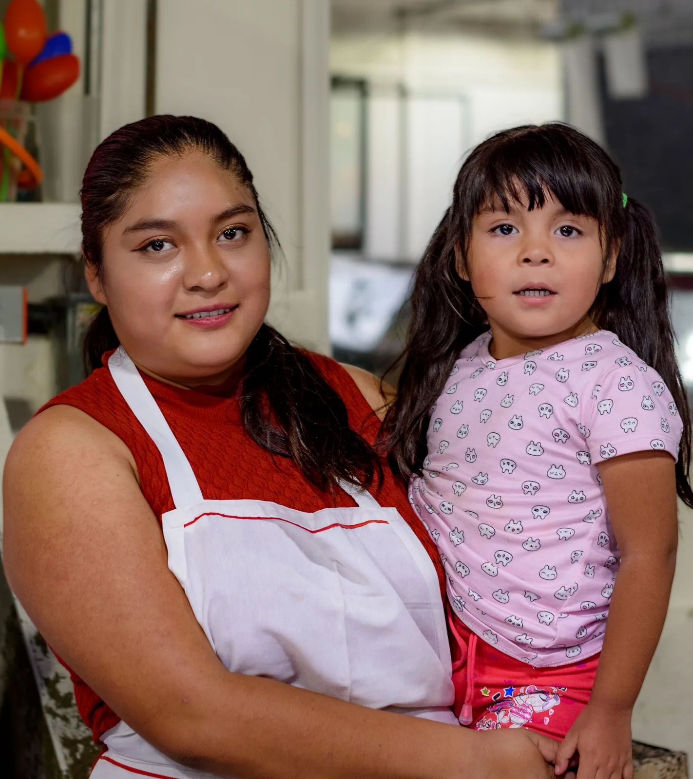 Smiling mother in an apron holding her young daughter inside their small shop