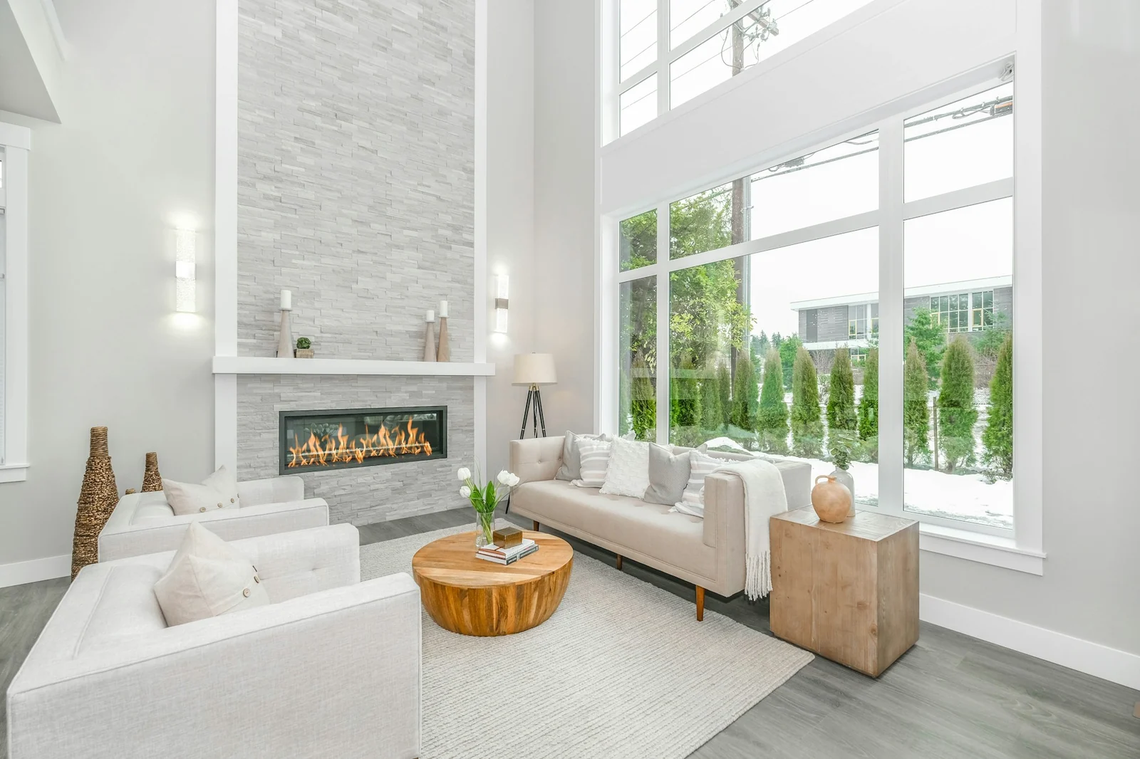 White living room with light sofas, stone fireplace and tall windows