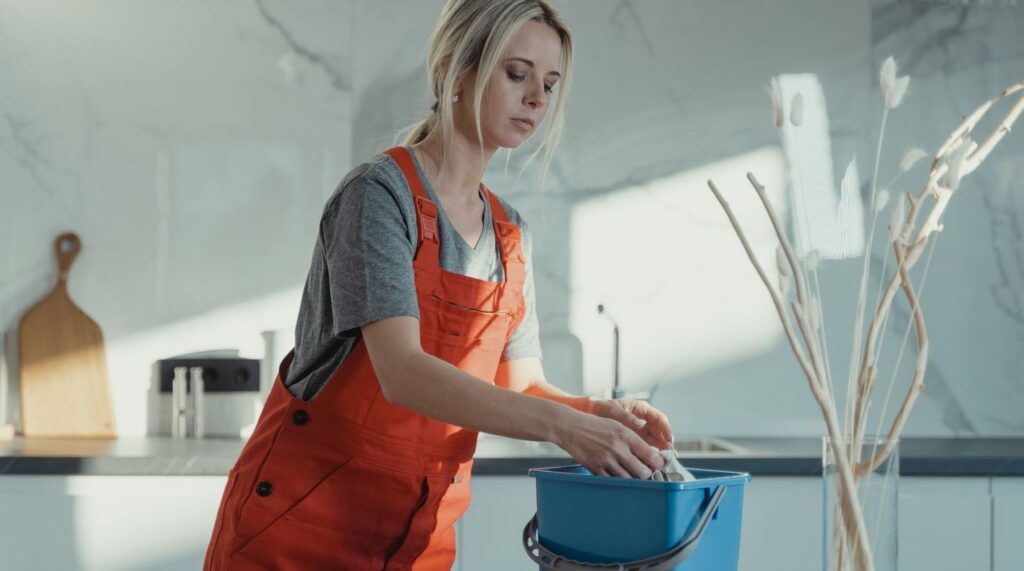 Cleaner wringing a cloth into a bucket in a bright marble kitchen